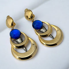 Vintage French modernist clip-on earrings with faceted blue round cabochons, layered gold and silver-tone metal crescents, and long sculptural dangles; shown from multiple angles to highlight texture, asymmetry, and mixed-metal design.