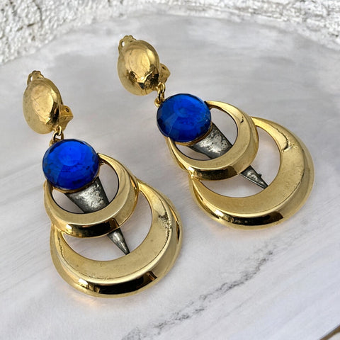 Vintage French modernist clip-on earrings with faceted blue round cabochons, layered gold and silver-tone metal crescents, and long sculptural dangles; shown from multiple angles to highlight texture, asymmetry, and mixed-metal design.