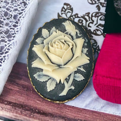 A lovely vintage French faux cameo scarf/dress clip from the late 1950s or early 1960s. Featuring a cream-colored high relief rose set against a black background, encased in a scalloped gold-tone bezel. The hammered gold frame adds texture, while the clip at the back ensures secure attachment to scarves, dresses, or lapels. Marked '3S' on the back, though the maker is unknown. A timeless and elegant accessory, perfect for vintage lovers and sustainable fashion enthusiasts.