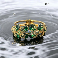 Vintage Juliana clamper bracelet from the 1950s, featuring 10 emerald-shaped rhinestones with filigree leaves, three AB light green rhinestones, and a gold-tone finish. A glamorous statement piece in excellent condition.