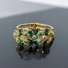 Vintage Juliana clamper bracelet from the 1950s, featuring 10 emerald-shaped rhinestones with filigree leaves, three AB light green rhinestones, and a gold-tone finish. A glamorous statement piece in excellent condition.