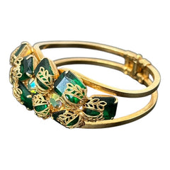 Vintage Juliana clamper bracelet from the 1950s, featuring 10 emerald-shaped rhinestones with filigree leaves, three AB light green rhinestones, and a gold-tone finish. A glamorous statement piece in excellent condition.