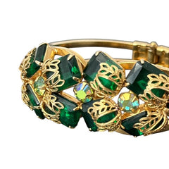 Vintage Juliana clamper bracelet from the 1950s, featuring 10 emerald-shaped rhinestones with filigree leaves, three AB light green rhinestones, and a gold-tone finish. A glamorous statement piece in excellent condition.