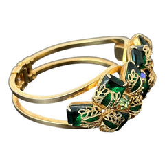 Vintage Juliana clamper bracelet from the 1950s, featuring 10 emerald-shaped rhinestones with filigree leaves, three AB light green rhinestones, and a gold-tone finish. A glamorous statement piece in excellent condition.