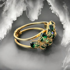 Vintage Juliana clamper bracelet from the 1950s, featuring 10 emerald-shaped rhinestones with filigree leaves, three AB light green rhinestones, and a gold-tone finish. A glamorous statement piece in excellent condition.