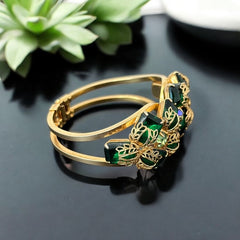 Vintage Juliana clamper bracelet from the 1950s, featuring 10 emerald-shaped rhinestones with filigree leaves, three AB light green rhinestones, and a gold-tone finish. A glamorous statement piece in excellent condition.