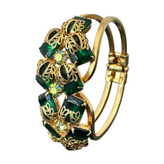 Vintage Juliana clamper bracelet from the 1950s, featuring 10 emerald-shaped rhinestones with filigree leaves, three AB light green rhinestones, and a gold-tone finish. A glamorous statement piece in excellent condition.