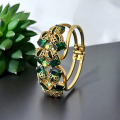 Vintage Juliana clamper bracelet from the 1950s, featuring 10 emerald-shaped rhinestones with filigree leaves, three AB light green rhinestones, and a gold-tone finish. A glamorous statement piece in excellent condition.