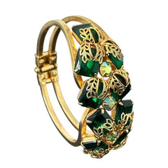 Vintage Juliana clamper bracelet from the 1950s, featuring 10 emerald-shaped rhinestones with filigree leaves, three AB light green rhinestones, and a gold-tone finish. A glamorous statement piece in excellent condition.