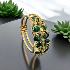 Vintage Juliana clamper bracelet from the 1950s, featuring 10 emerald-shaped rhinestones with filigree leaves, three AB light green rhinestones, and a gold-tone finish. A glamorous statement piece in excellent condition.