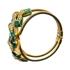 Vintage Juliana clamper bracelet from the 1950s, featuring 10 emerald-shaped rhinestones with filigree leaves, three AB light green rhinestones, and a gold-tone finish. A glamorous statement piece in excellent condition.