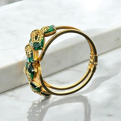 Vintage Juliana clamper bracelet from the 1950s, featuring 10 emerald-shaped rhinestones with filigree leaves, three AB light green rhinestones, and a gold-tone finish. A glamorous statement piece in excellent condition.