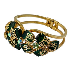 Vintage Juliana clamper bracelet from the 1950s, featuring 10 emerald-shaped rhinestones with filigree leaves, three AB light green rhinestones, and a gold-tone finish. A glamorous statement piece in excellent condition.