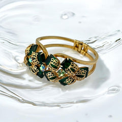 Vintage Juliana clamper bracelet from the 1950s, featuring 10 emerald-shaped rhinestones with filigree leaves, three AB light green rhinestones, and a gold-tone finish. A glamorous statement piece in excellent condition.