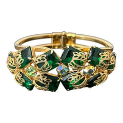 Vintage Juliana clamper bracelet from the 1950s, featuring 10 emerald-shaped rhinestones with filigree leaves, three AB light green rhinestones, and a gold-tone finish. A glamorous statement piece in excellent condition.