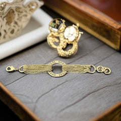 Gold tone Guess bracelet with multi-strand chains and a central ring engraved with ‘GUESS’ and accented by clear rhinestones, shown on neutral backdrop.