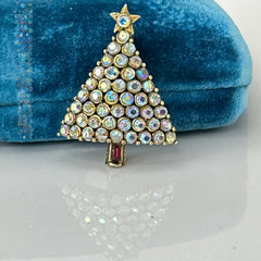 Vintage Hollycraft Christmas tree brooch with clear Aurora Borealis rhinestones in a gold-tone setting, featuring a gold star at the top and a red rhinestone base. Signed on the reverse and measuring approximately 1 3/8 inches tall by 1 inch wide.