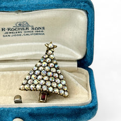Vintage Hollycraft Christmas tree brooch with clear Aurora Borealis rhinestones in a gold-tone setting, featuring a gold star at the top and a red rhinestone base. Signed on the reverse and measuring approximately 1 3/8 inches tall by 1 inch wide.