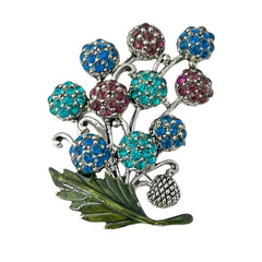 Vintage Hollycraft rhinestone brooch from the 1950s/60s featuring 10 multicolor rhinestone berries in blue, teal green, and dark amethyst hues on silver-tone branches, accented by a green enamel leaf with a small spot of missing enamel at the bottom.