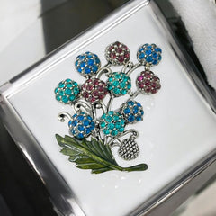 Vintage Hollycraft rhinestone brooch from the 1950s/60s featuring 10 multicolor rhinestone berries in blue, teal green, and dark amethyst hues on silver-tone branches, accented by a green enamel leaf with a small spot of missing enamel at the bottom.