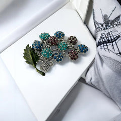 Vintage Hollycraft rhinestone brooch from the 1950s/60s featuring 10 multicolor rhinestone berries in blue, teal green, and dark amethyst hues on silver-tone branches, accented by a green enamel leaf with a small spot of missing enamel at the bottom.