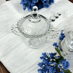 A vintage Imperial Candlewick pattern glass condiment jar set, featuring a handled jar, a fitted glass lid, and a matching glass spoon. Made between 1936 and 1984, the set is in excellent vintage condition and showcases the iconic bead design of the Candlewick collection.