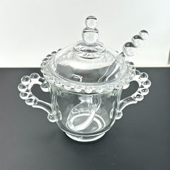 A vintage Imperial Candlewick pattern glass condiment jar set, featuring a handled jar, a fitted glass lid, and a matching glass spoon. Made between 1936 and 1984, the set is in excellent vintage condition and showcases the iconic bead design of the Candlewick collection.