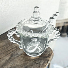 A vintage Imperial Candlewick pattern glass condiment jar set, featuring a handled jar, a fitted glass lid, and a matching glass spoon. Made between 1936 and 1984, the set is in excellent vintage condition and showcases the iconic bead design of the Candlewick collection.