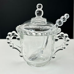 A vintage Imperial Candlewick pattern glass condiment jar set, featuring a handled jar, a fitted glass lid, and a matching glass spoon. Made between 1936 and 1984, the set is in excellent vintage condition and showcases the iconic bead design of the Candlewick collection.