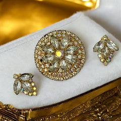 Verified Juliana #1402 vintage clear rhinestone and gold-tone floral brooch with matching clip-on earrings. The brooch features dimensional layered rings of clear chaton and AB rhinestones, with marquise rhinestones encircling the center. Earrings showcase a leaf-shaped design with marquise rhinestones and AB chaton accents. Mid-century elegance from the late 1950s or early 1960s.