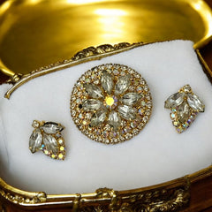 Verified Juliana #1402 vintage clear rhinestone and gold-tone floral brooch with matching clip-on earrings. The brooch features dimensional layered rings of clear chaton and AB rhinestones, with marquise rhinestones encircling the center. Earrings showcase a leaf-shaped design with marquise rhinestones and AB chaton accents. Mid-century elegance from the late 1950s or early 1960s.