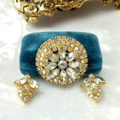 Verified Juliana #1402 vintage clear rhinestone and gold-tone floral brooch with matching clip-on earrings. The brooch features dimensional layered rings of clear chaton and AB rhinestones, with marquise rhinestones encircling the center. Earrings showcase a leaf-shaped design with marquise rhinestones and AB chaton accents. Mid-century elegance from the late 1950s or early 1960s.
