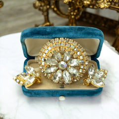 Verified Juliana #1402 vintage clear rhinestone and gold-tone floral brooch with matching clip-on earrings. The brooch features dimensional layered rings of clear chaton and AB rhinestones, with marquise rhinestones encircling the center. Earrings showcase a leaf-shaped design with marquise rhinestones and AB chaton accents. Mid-century elegance from the late 1950s or early 1960s.