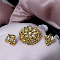 Verified Juliana #1402 vintage clear rhinestone and gold-tone floral brooch with matching clip-on earrings. The brooch features dimensional layered rings of clear chaton and AB rhinestones, with marquise rhinestones encircling the center. Earrings showcase a leaf-shaped design with marquise rhinestones and AB chaton accents. Mid-century elegance from the late 1950s or early 1960s.