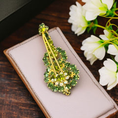Vintage Juliana violin brooch in gold tone metal with green and peridot rhinestones, featuring layered construction and floral accents; verified design #3151 from the 1960s, shown from front and back.