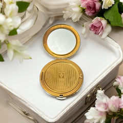 Vintage 1950s Kigu gold-tone powder compact with guilloché moiré lid, original puff, and mirror—collectible beauty accessory with timeless charm.