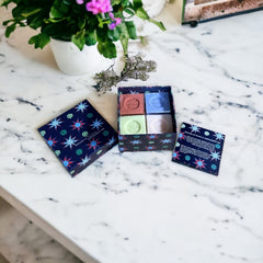 Gift box featuring a charming Moon and Sun design on a midnight blue background. Contains four artisanal Marseille cube soaps in Violet, Rose, Verbena, and Red Berries fragrances.