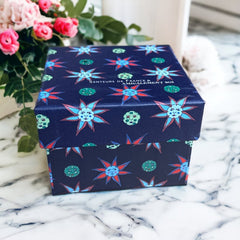 Gift box featuring a charming Moon and Sun design on a midnight blue background. Contains four artisanal Marseille cube soaps in Violet, Rose, Verbena, and Red Berries fragrances.