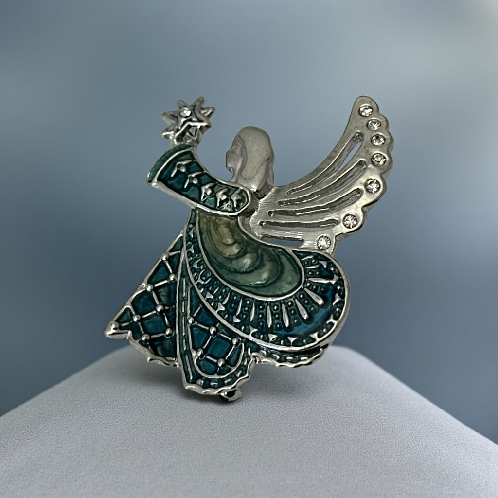 Vintage Monet angel brooch in silver tone metal with teal and light green enamel robe, clear rhinestone wings, and raised star detail; signed Monet on back.