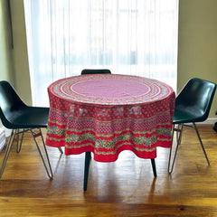 Round Provence-style cotton tablecloth by Le Cluny, featuring a vibrant red background with yellow mimosa and black olive detailing. Measures 70 inches in diameter, made in France, suitable for indoor and outdoor use, and machine washable for easy care.