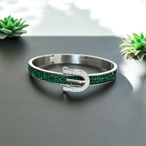 Emerald and clear rhinestone hinged bangle bracelet made of polished stainless steel with a modern belt buckle design, featuring sparkling accents and marked 316L S.Steel, photographed in excellent condition.