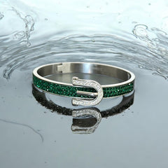 Emerald and clear rhinestone hinged bangle bracelet made of polished stainless steel with a modern belt buckle design, featuring sparkling accents and marked 316L S.Steel, photographed in excellent condition.