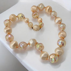 Vintage 1950s/1960s single-strand necklace featuring light peach hollow plastic beads alternating between opaque satin and iridescent transparent beads, finished with a snap clasp adorned with a light peach satin cabochon, signed Japan, in very good vintage condition.