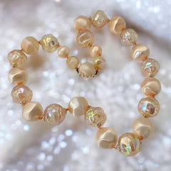 Vintage 1950s/1960s single-strand necklace featuring light peach hollow plastic beads alternating between opaque satin and iridescent transparent beads, finished with a snap clasp adorned with a light peach satin cabochon, signed Japan, in very good vintage condition.