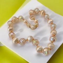 Vintage 1950s/1960s single-strand necklace featuring light peach hollow plastic beads alternating between opaque satin and iridescent transparent beads, finished with a snap clasp adorned with a light peach satin cabochon, signed Japan, in very good vintage condition.