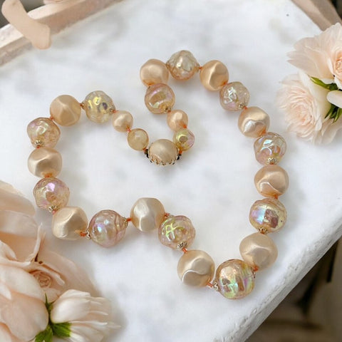 Vintage 1950s/1960s single-strand necklace featuring light peach hollow plastic beads alternating between opaque satin and iridescent transparent beads, finished with a snap clasp adorned with a light peach satin cabochon, signed Japan, in very good vintage condition.