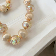 Vintage 1950s/1960s single-strand necklace featuring light peach hollow plastic beads alternating between opaque satin and iridescent transparent beads, finished with a snap clasp adorned with a light peach satin cabochon, signed Japan, in very good vintage condition.
