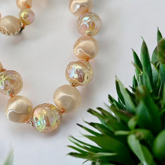 Vintage 1950s/1960s single-strand necklace featuring light peach hollow plastic beads alternating between opaque satin and iridescent transparent beads, finished with a snap clasp adorned with a light peach satin cabochon, signed Japan, in very good vintage condition.