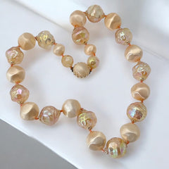 Vintage 1950s/1960s single-strand necklace featuring light peach hollow plastic beads alternating between opaque satin and iridescent transparent beads, finished with a snap clasp adorned with a light peach satin cabochon, signed Japan, in very good vintage condition.