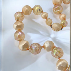 Vintage 1950s/1960s single-strand necklace featuring light peach hollow plastic beads alternating between opaque satin and iridescent transparent beads, finished with a snap clasp adorned with a light peach satin cabochon, signed Japan, in very good vintage condition.